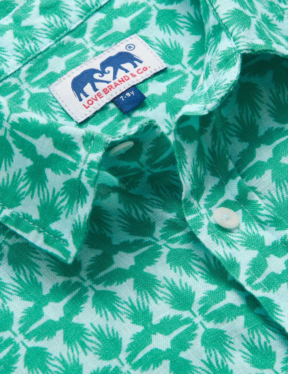 Close-up of Boys Palm Eagle Abaco Linen Shirt showcasing green tropical palm leaves and eagles design with brand label and buttons.