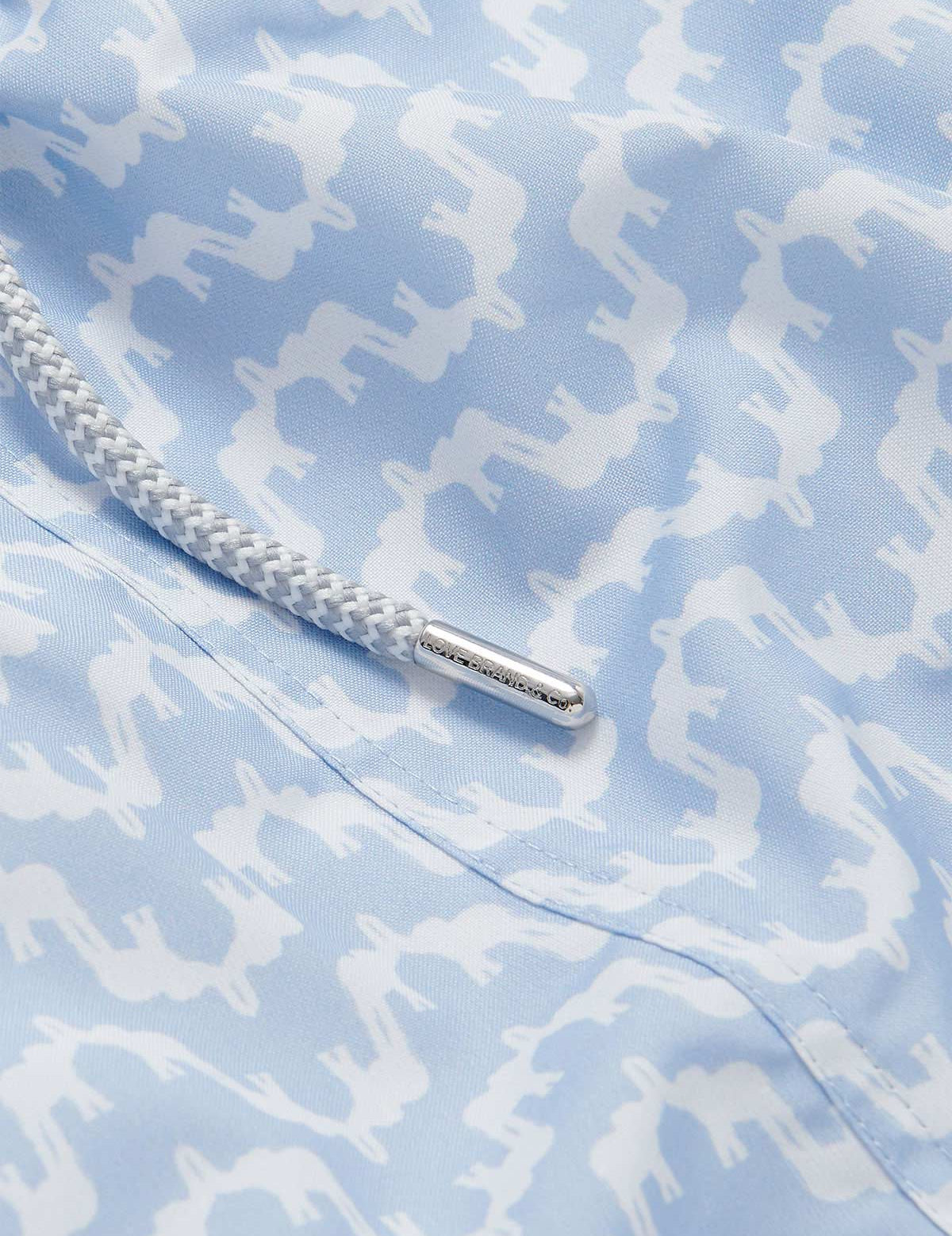 Close-up of the Men's Elephant Palace Sky Staniel Swim Shorts. Patterned swim shorts showcasing a sky blue fabric with white elephant and palace patterns, along with a braided drawstring.