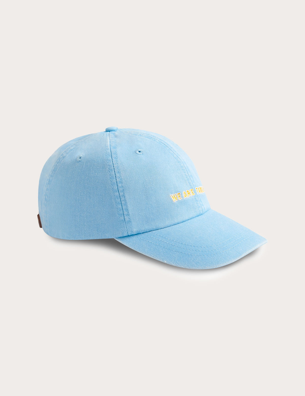 Sky blue cotton peak cap with 'We Are Family' embroidery on the front, featuring a leather strap and brass adjuster.