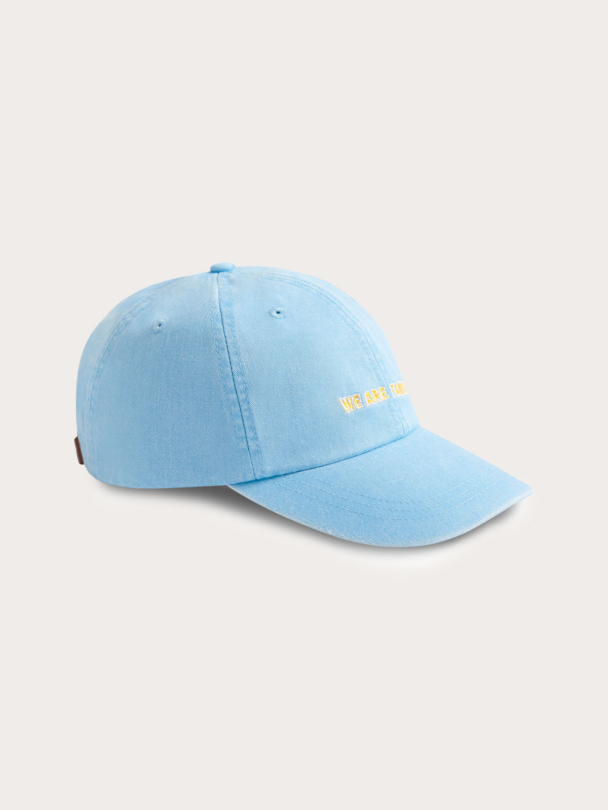 Sky blue cotton peak cap with 'We Are Family' embroidery on the front, featuring a leather strap and brass adjuster.