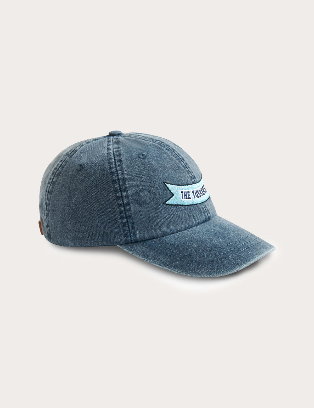 Soft cotton peak cap in washed navy blue featuring ‘The Tuskers’ ribbon embroidery on the front, with leather strap and brass adjuster.