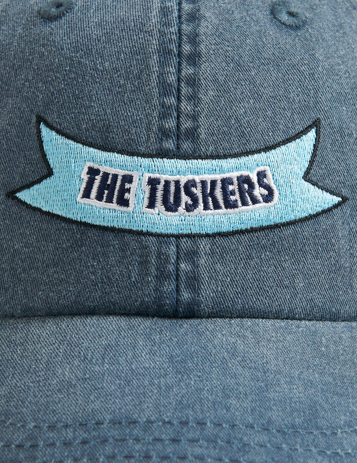 The Tuskers' Cap in washed navy featuring 'The Tuskers' ribbon embroidery on the front.