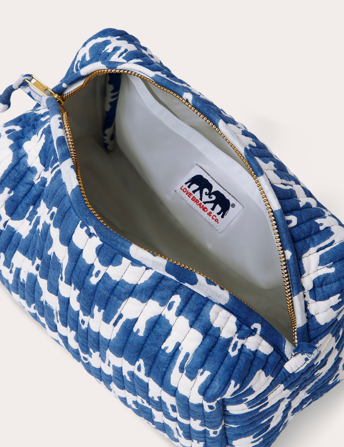 Quilted wash bag in blue with white elephant print, featuring a zippered opening and lined interior with a pocket.