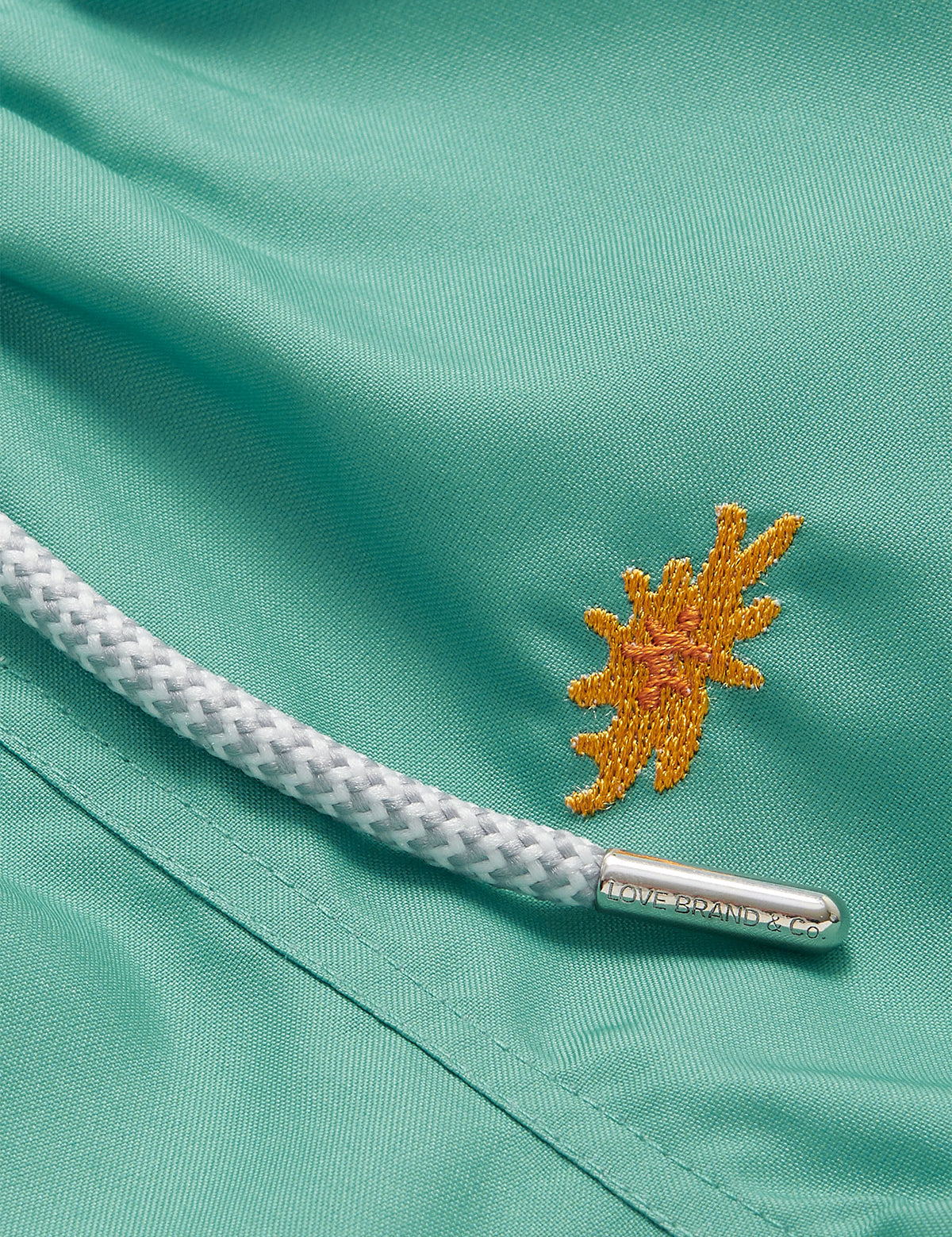 Close-up of Boys Primavera Staniel Swim Shorts in riviera green with embroidered sea flower detail and drawstring.