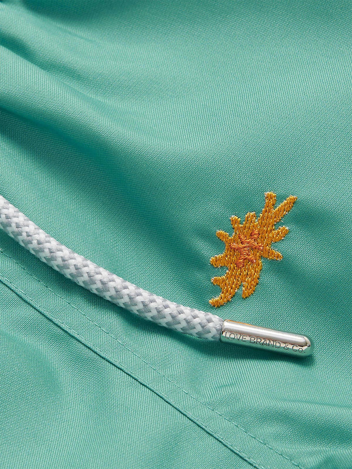 Close-up of Boys Primavera Staniel Swim Shorts in riviera green with embroidered sea flower detail and drawstring.