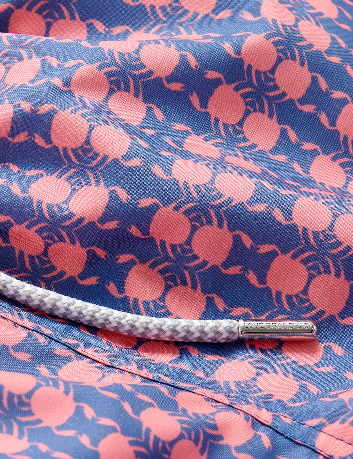 Close-up of Boys Crab Pool Staniel Swim Shorts featuring pink crab and watermelon pattern on a deep blue background with a white drawstring.