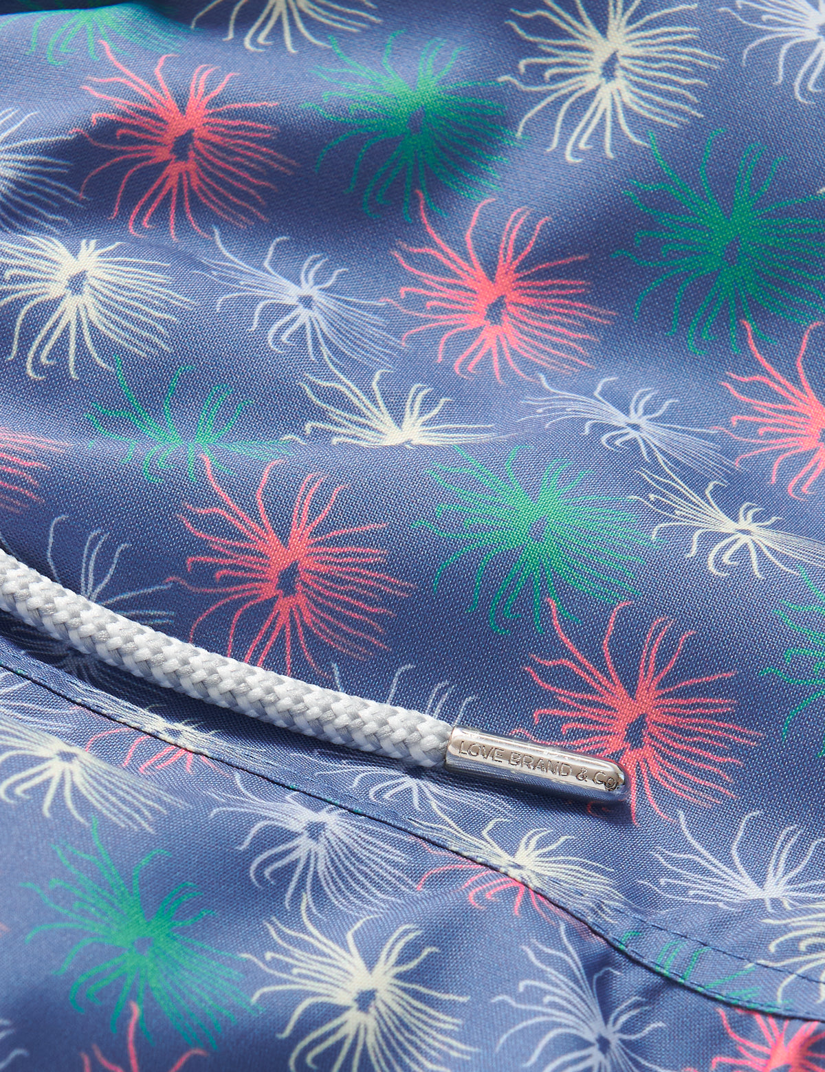 Close-up view of Boys Dont be Anemone Staniel Swim Shorts, showcasing colorful sea anemone patterns on blue fabric, with a white drawstring detail.