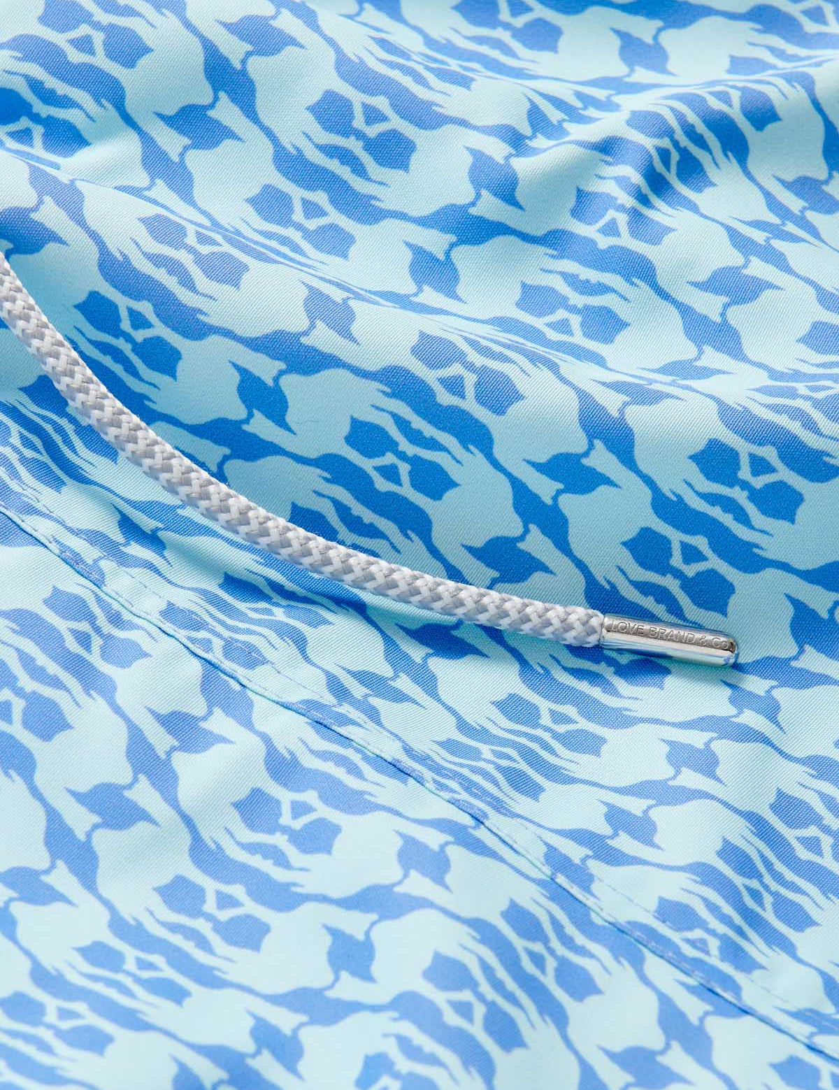 Close-up view of Boys Camel Mirage Sky Staniel Swim Shorts with a blue and white mirage pattern, highlighting the bespoke design celebrating Cop28 in Dubai 2023.