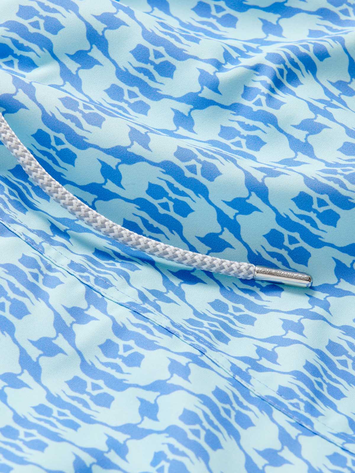 Close-up view of Boys Camel Mirage Sky Staniel Swim Shorts with a blue and white mirage pattern, highlighting the bespoke design celebrating Cop28 in Dubai 2023.