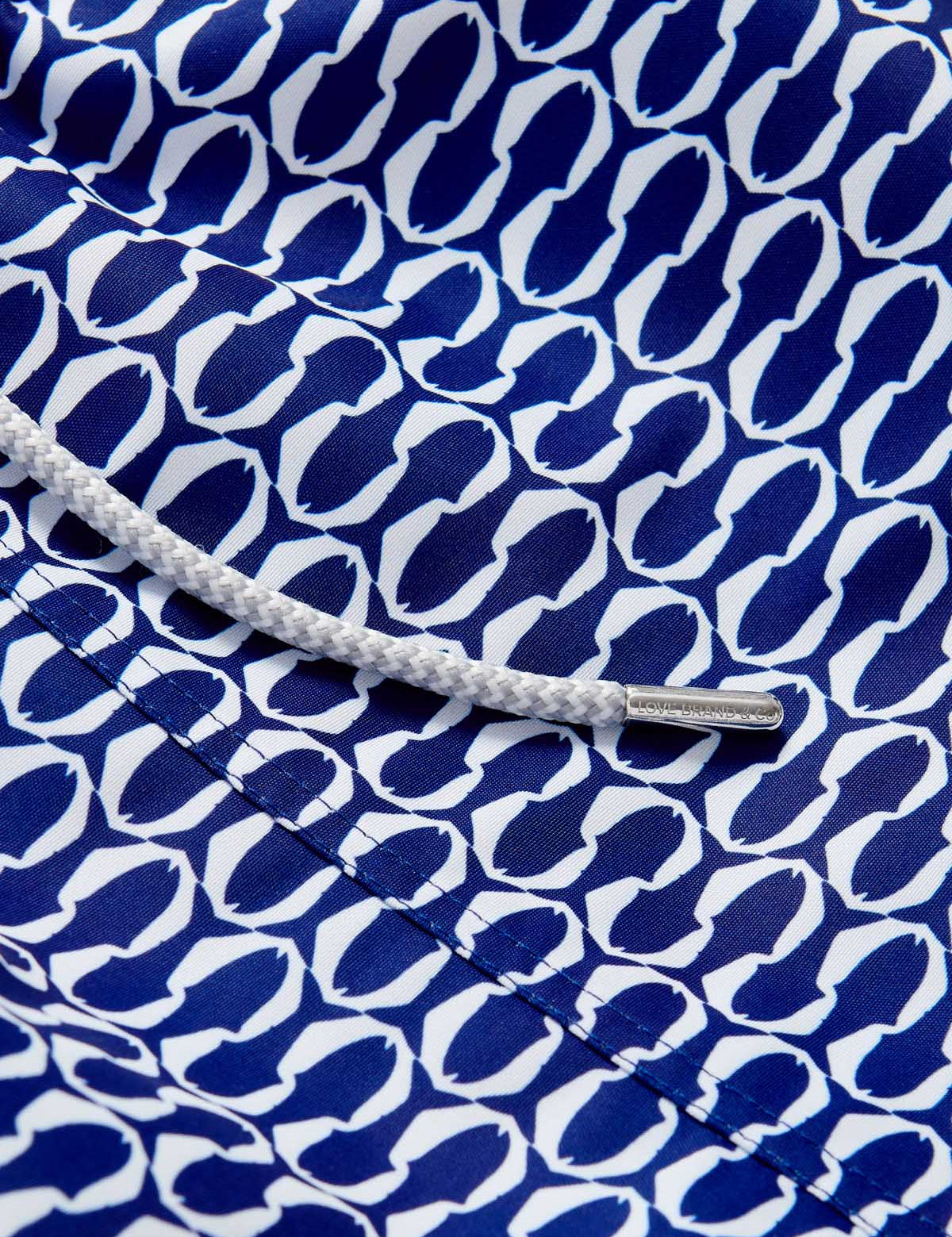 Close-up view of the Boys Pine Cay Fish Staniel Swim Shorts showcasing a sleek geometric print of blue and white fish silhouettes with a white drawstring.