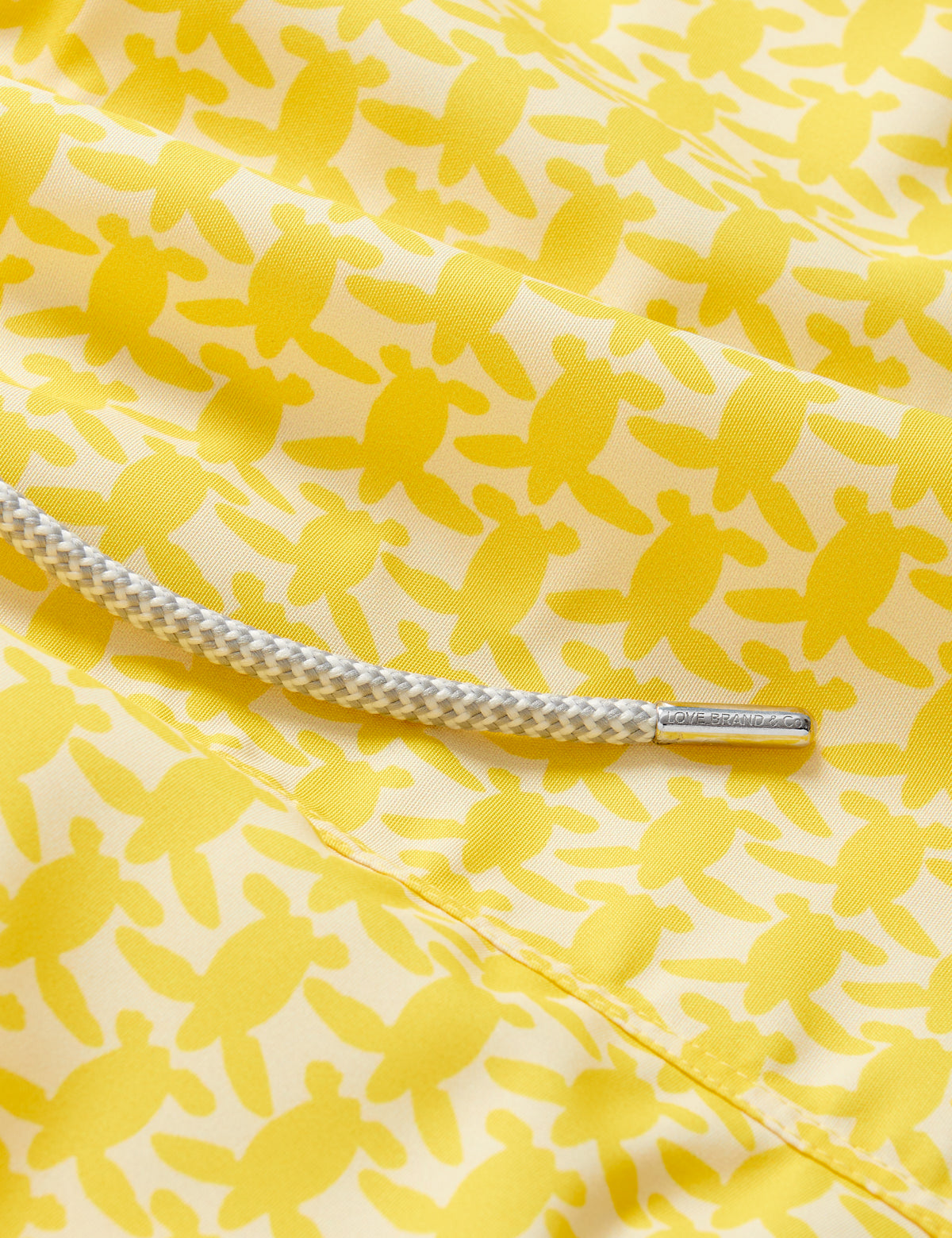 Yellow swim shorts with an all-over turtle print pattern, dedicated to raising awareness about the endangered turtles in Barbados, featuring a white drawstring cord.