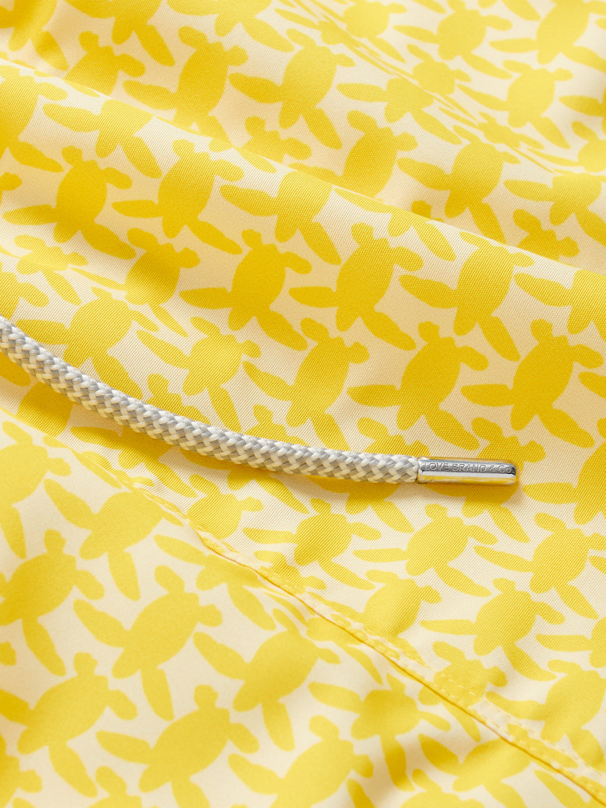 Yellow swim shorts with an all-over turtle print pattern, dedicated to raising awareness about the endangered turtles in Barbados, featuring a white drawstring cord.