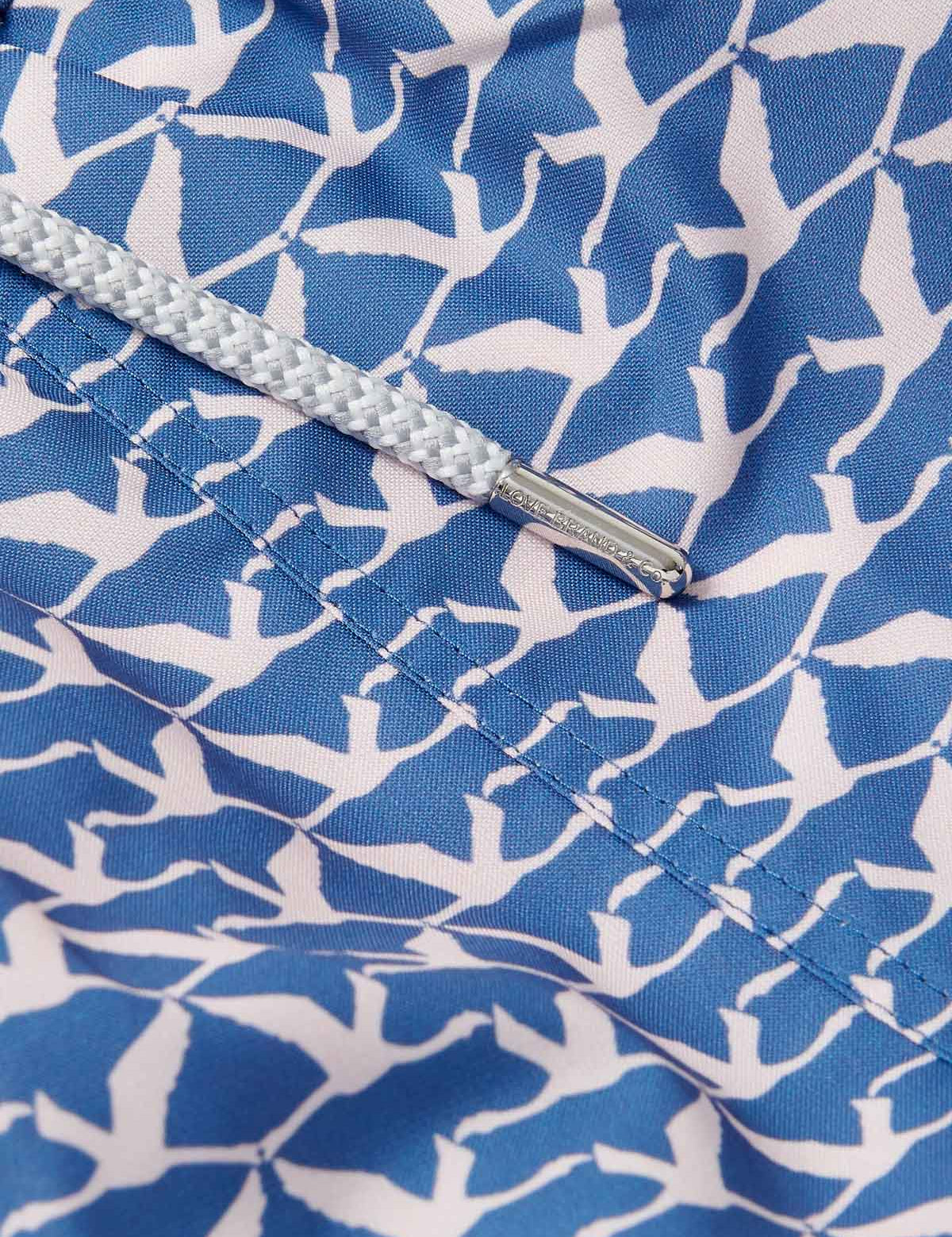 Close-up image of the Men's Flamingo Flamboyance Staniel Swim Shorts. Patterned swim shorts featuring a blue and white flamingo print pattern, highlighting the intricate stitching and a cord detail.