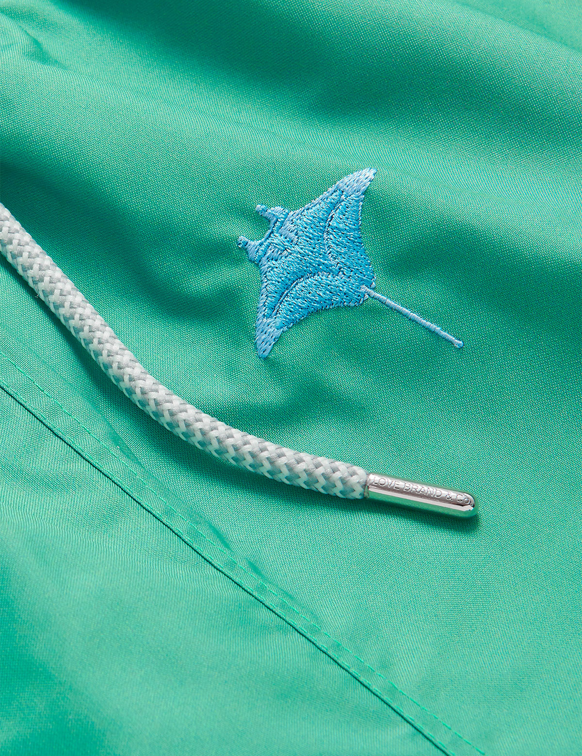 Close-up of the Men's Manta Migration Embroidered Staniel Swim Shorts showcasing the detailed manta ray embroidery on lightweight green fabric with a braided drawstring.