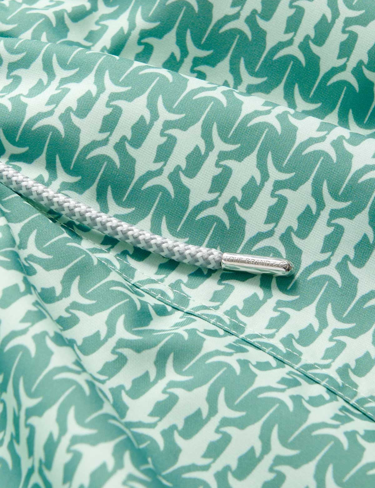 Close-up view of Men's Angarde Staniel Swim Shorts, featuring a swordfish pattern in soft green hues. Image of patterned swim shorts with a focus on the quality fabric and drawstring detail.