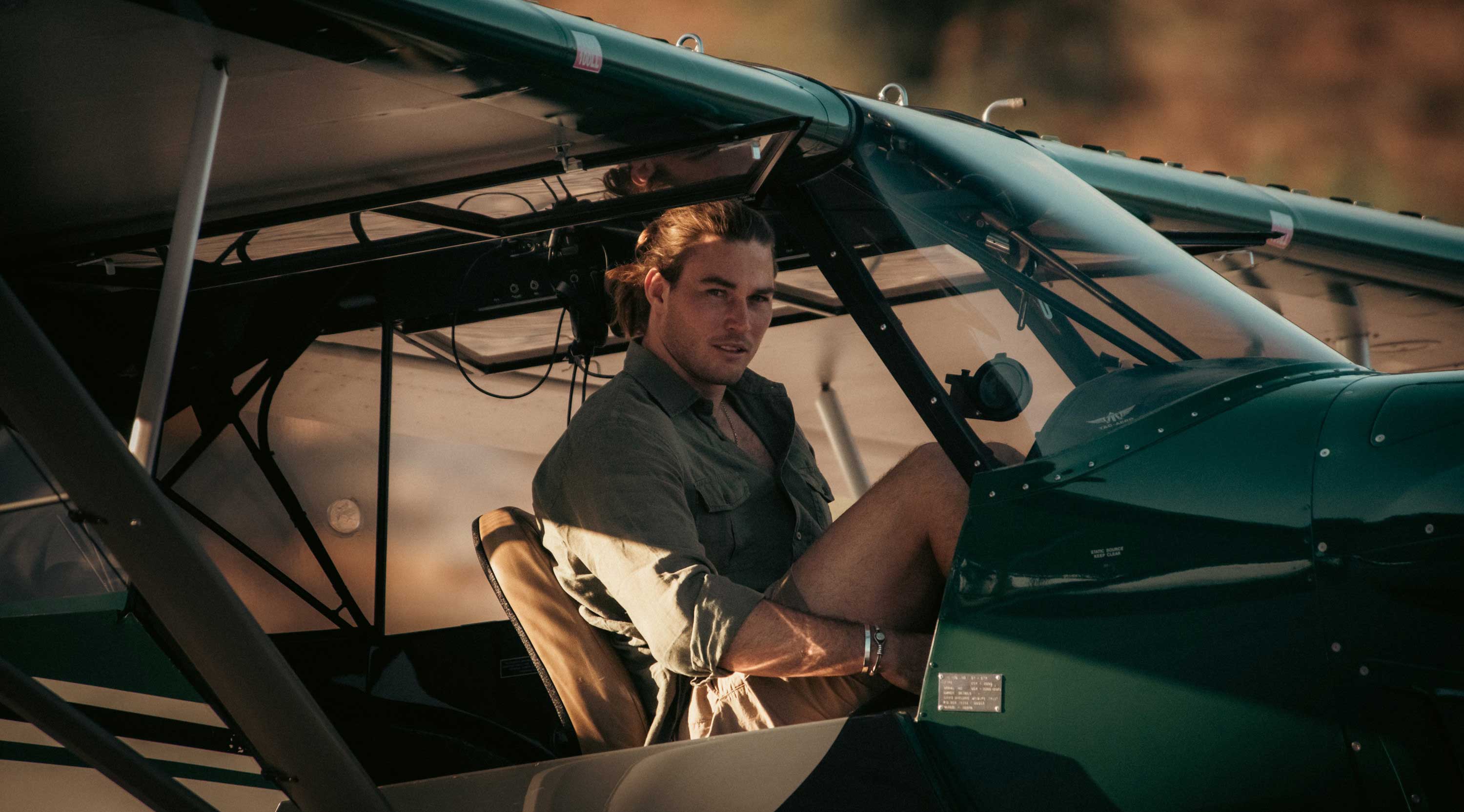 Roan Carr-Hartley in his plane for Sheldrick Wildlife Trust wearing LOVE BRAND & Co. Men's Olive Andros Hemp Shirt & Men's Stone Burrow Linen Shorts.