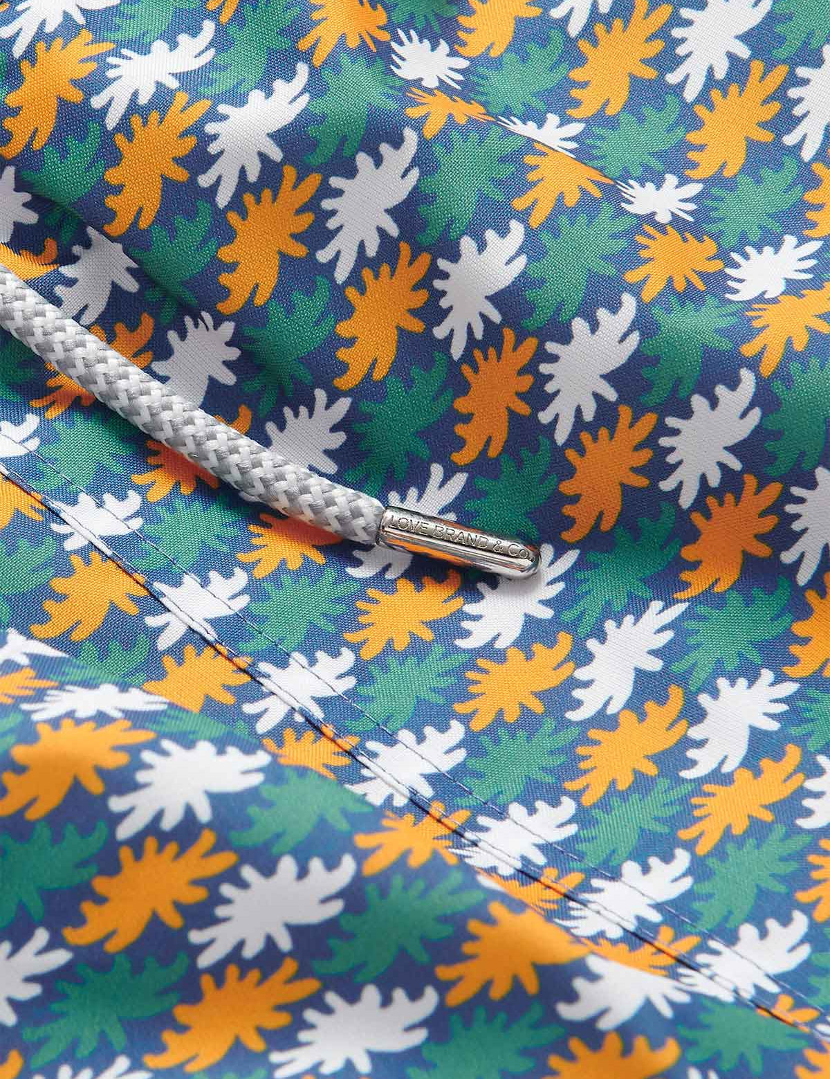 Close-up view of Men's Sea Flowers Staniel Swim Shorts featuring a pattern of ochre, white, and green sea anemones on a deep blue background, with a detailed braided drawstring.