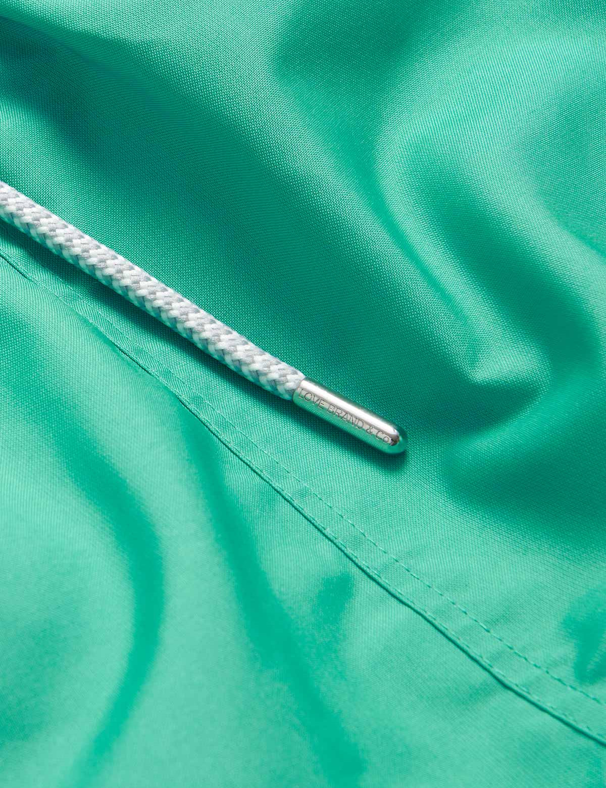 Close-up of Men's Sicilian Green Staniel Swim Shorts in vibrant green fabric showing a white drawstring with silver aglet.