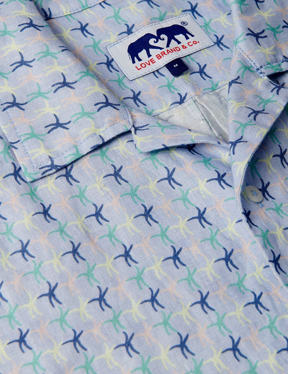 Close-up view of Star Dancer Arawak mens Linen Shirt featuring a pastel pink, limoncello, cay green, and deep blue sea star motif on a soothing ocean blue background.