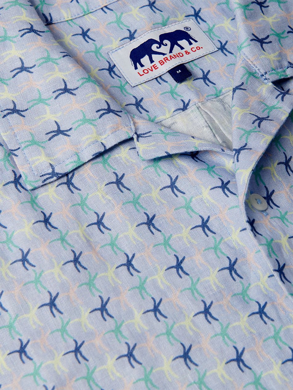 Close-up view of Star Dancer Arawak mens Linen Shirt featuring a pastel pink, limoncello, cay green, and deep blue sea star motif on a soothing ocean blue background.